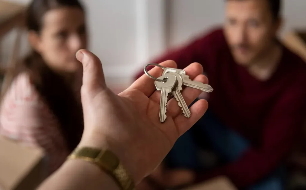 Mano sosteniendo un juego de llaves con una pareja en segundo plano